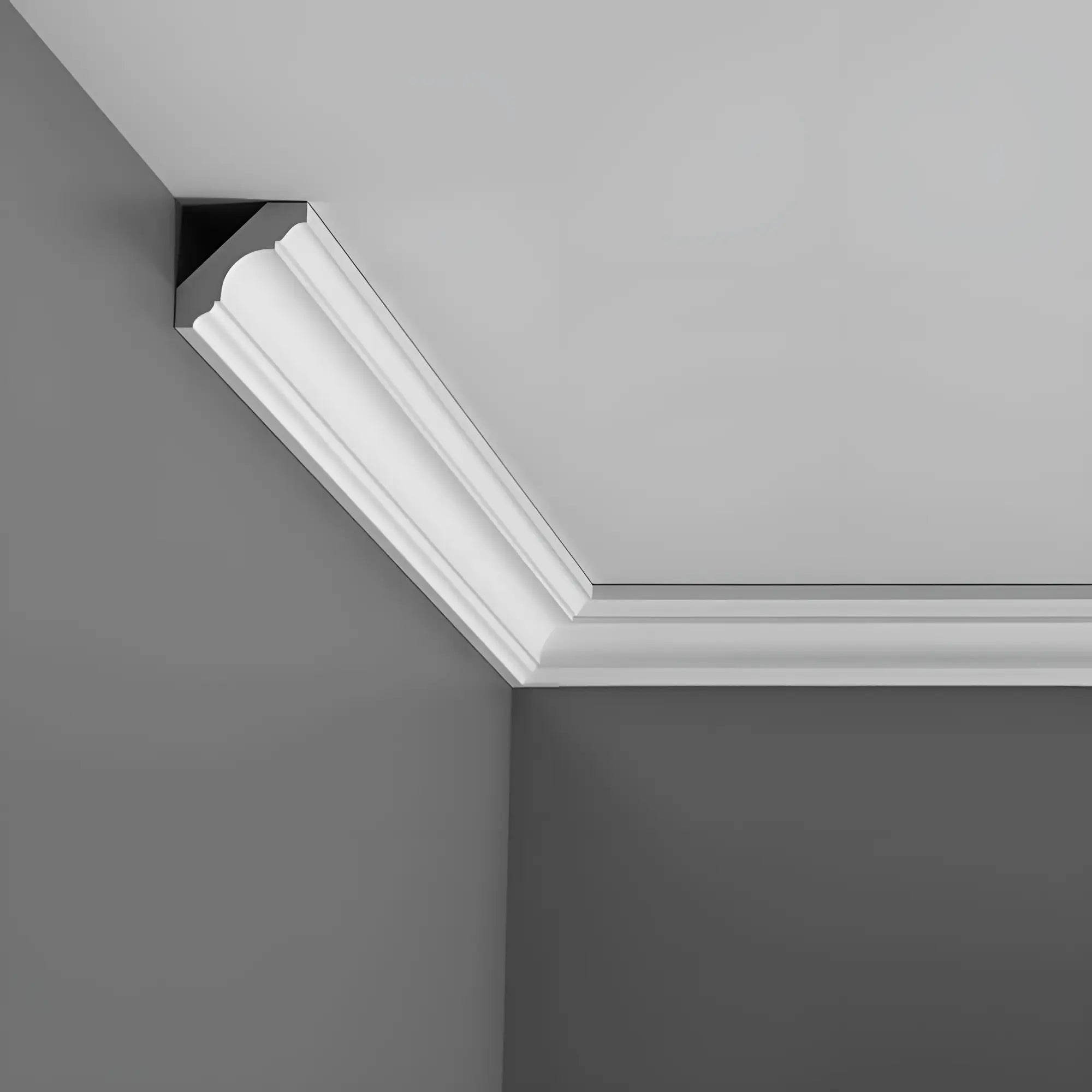 Ein modernes Interieur zeigt weiße Zierleisten aus der Purotouch-Reihe von Orac Decor an einer grauen Wand, die den Übergang zwischen Wand und Decke betonen. Die Stuckleiste besticht durch ein schlichtes, elegantes Design, das klare Linien und eine glatte Oberfläche betont und sich somit ideal für anspruchsvolle Raumgestaltung eignet.