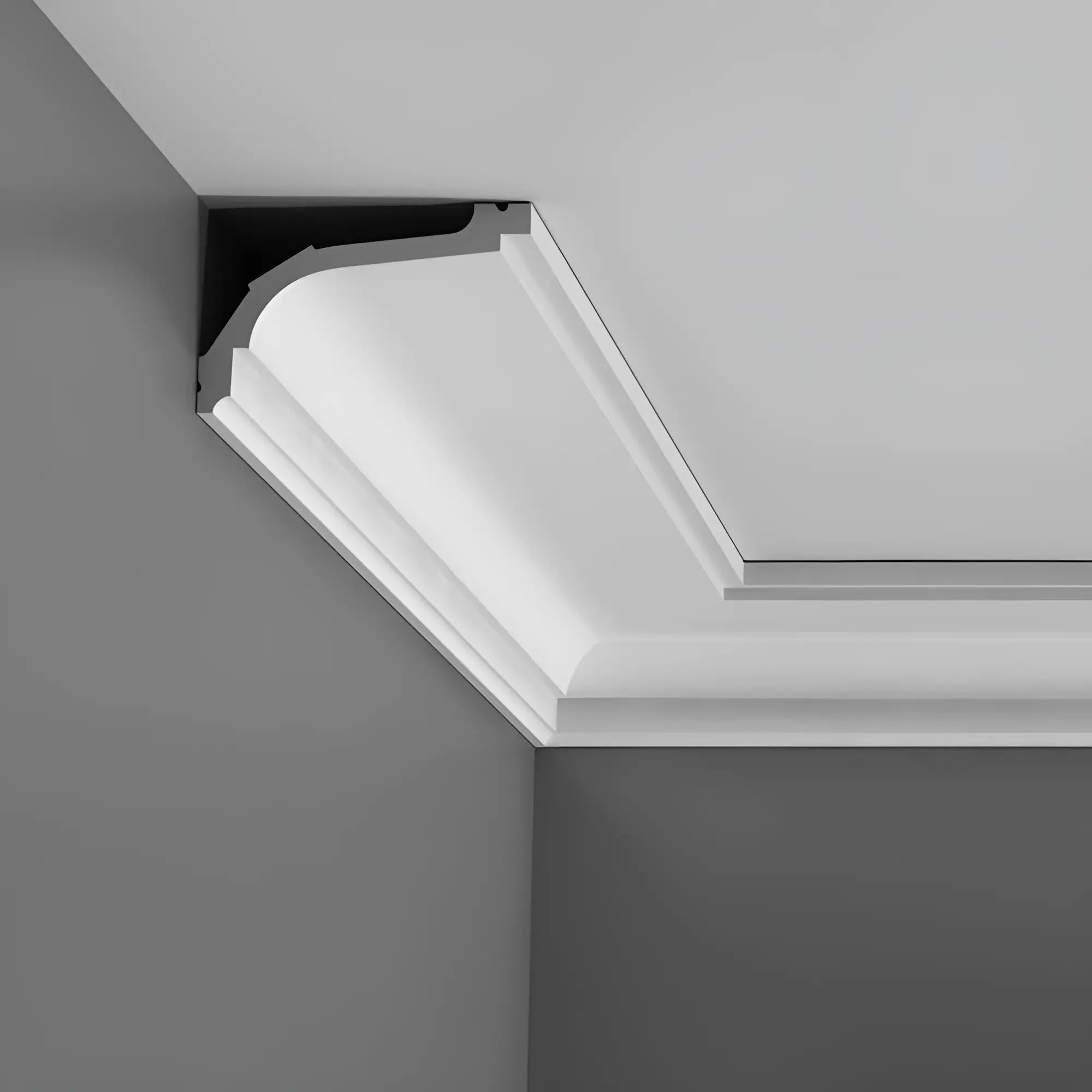 Nahaufnahme einer eleganten Deckenleiste mit einer klassischen Stuckleiste von Orac Decor mit klassischer, weißer, geschwungener Zierleiste vor einer grauen Wand, die einen stilvollen und raffinierten Übergang zwischen Wand und Decke schafft.