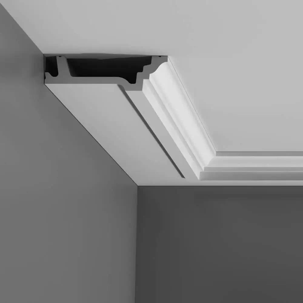 Nahaufnahme einer Deckenleiste mit modernem, geometrischem Design. Die Orac Decor Purotouch-Leiste wird an der Verbindung von Decke und Wand angebracht und zeichnet sich durch klare Linien und eine glatte weiße Oberfläche aus, die einen Kontrast zur dunkleren Wandfarbe bildet.