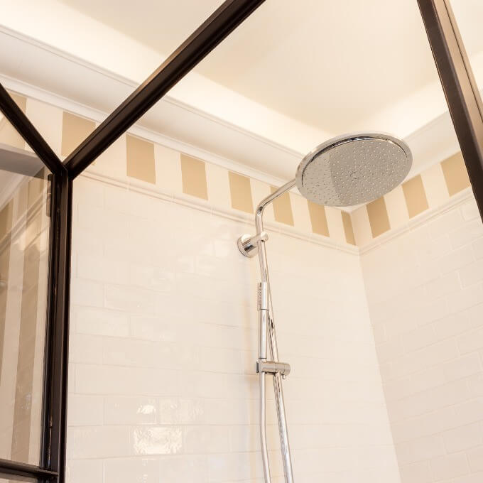 Eine moderne Dusche mit einem großzügigen runden Regenduschkopf und einem schicken Metallrahmen, hervorgehoben durch vielseitige Stuckleisten-Akzente von Orac Decor. Die Wände sind mit weißen Fliesen geschmückt, ergänzt durch eine dekorative beige Bordüre, ideal für eine elegante Raumgestaltung.