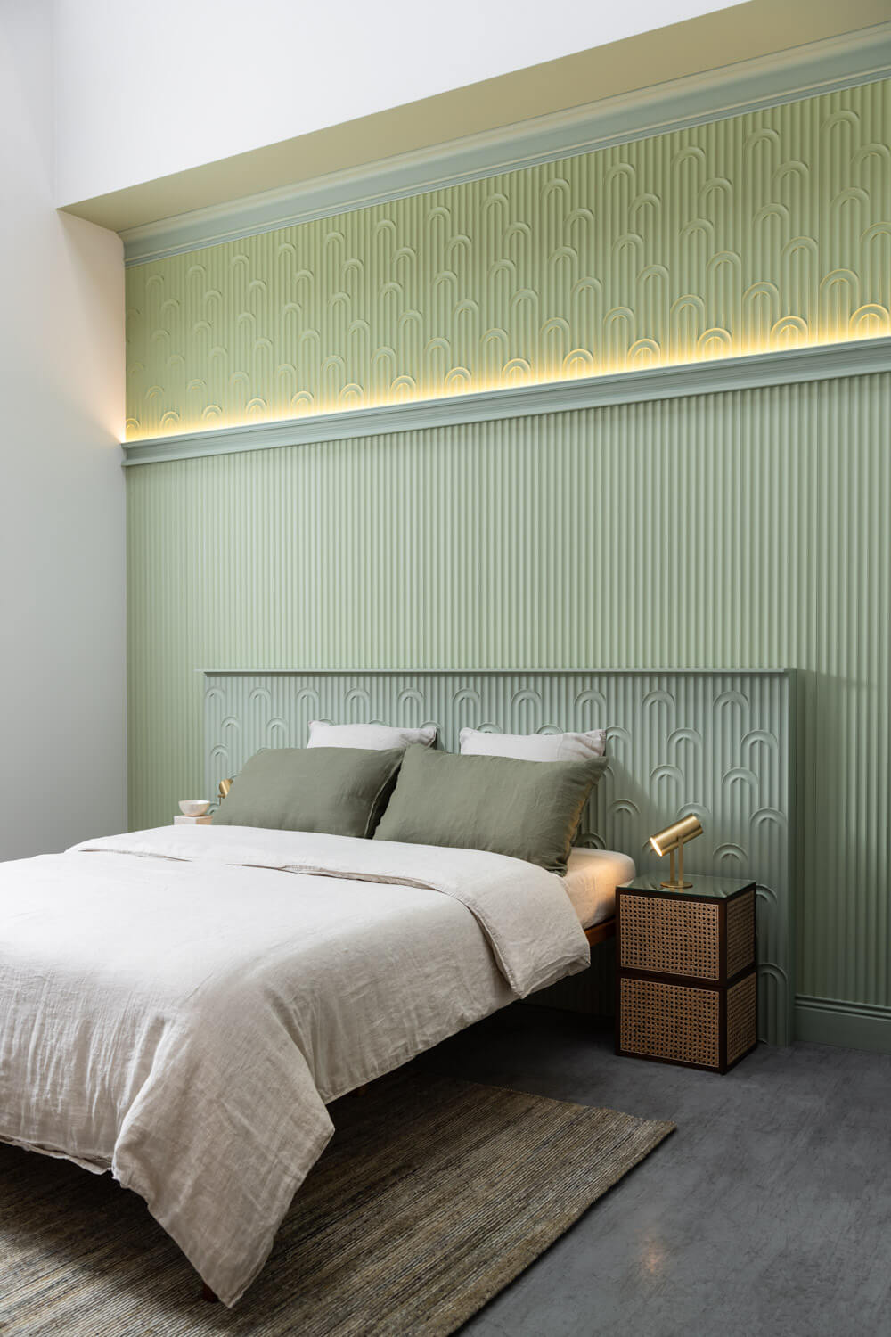 Ein minimalistisches Schlafzimmer mit einer grünen Akzentwand zeigt geometrische Muster und strahlt klassische Eleganz aus. Das Bett mit weißer und grüner Bettwäsche steht zwischen kleinen hölzernen Nachttischen mit Lampen. Sanft gefiltertes Tageslicht bringt die C339 NOBLESSE Stuckleiste von Orac Decor, gefertigt aus Purotouch, zur Geltung.